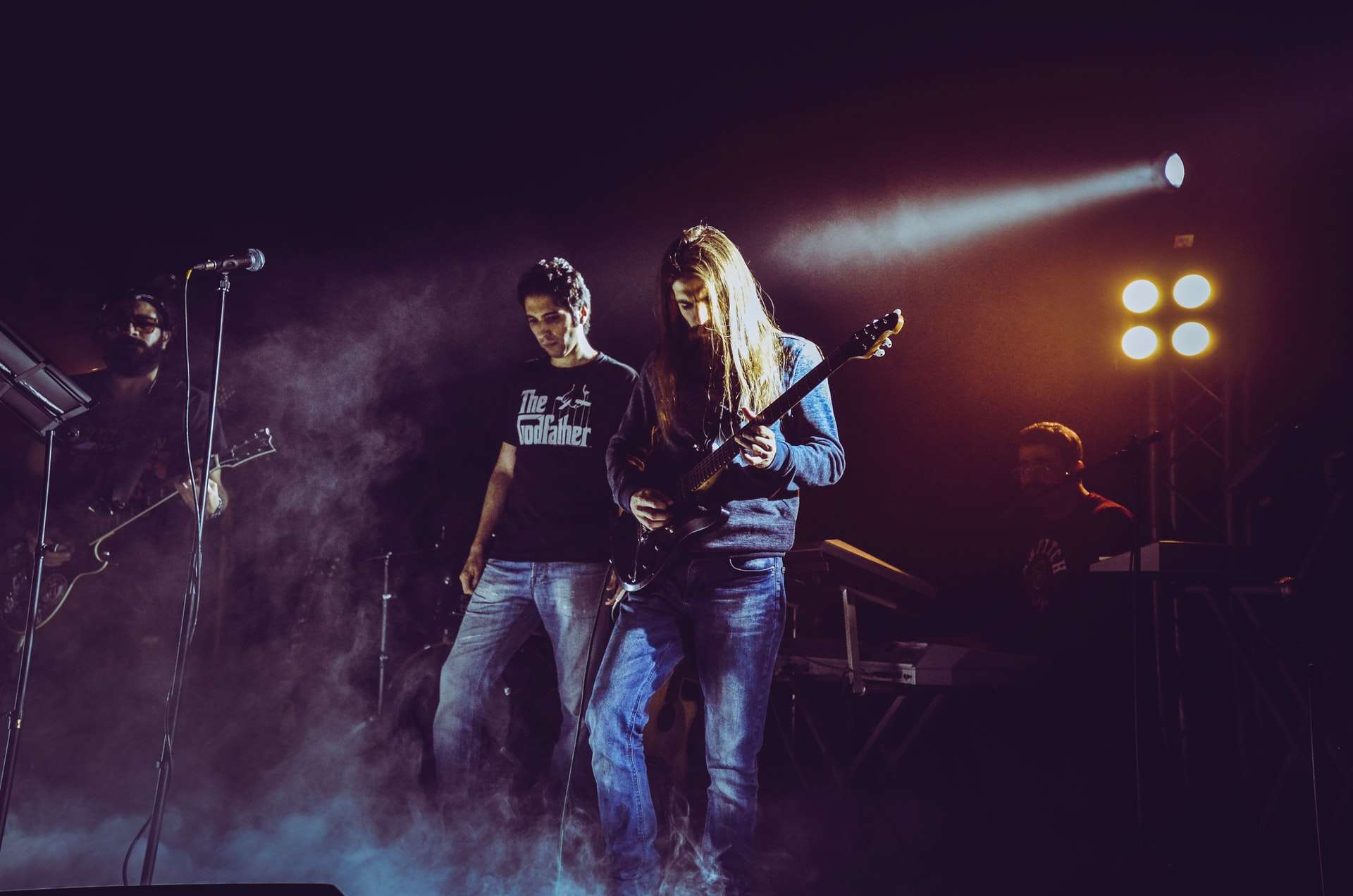 Un groupe de musique a répondu à une annonce et joue sur scène avec deux guitaristes, un chanteur et un pianiste éclairé par un projecteur dans un écran de fumée.