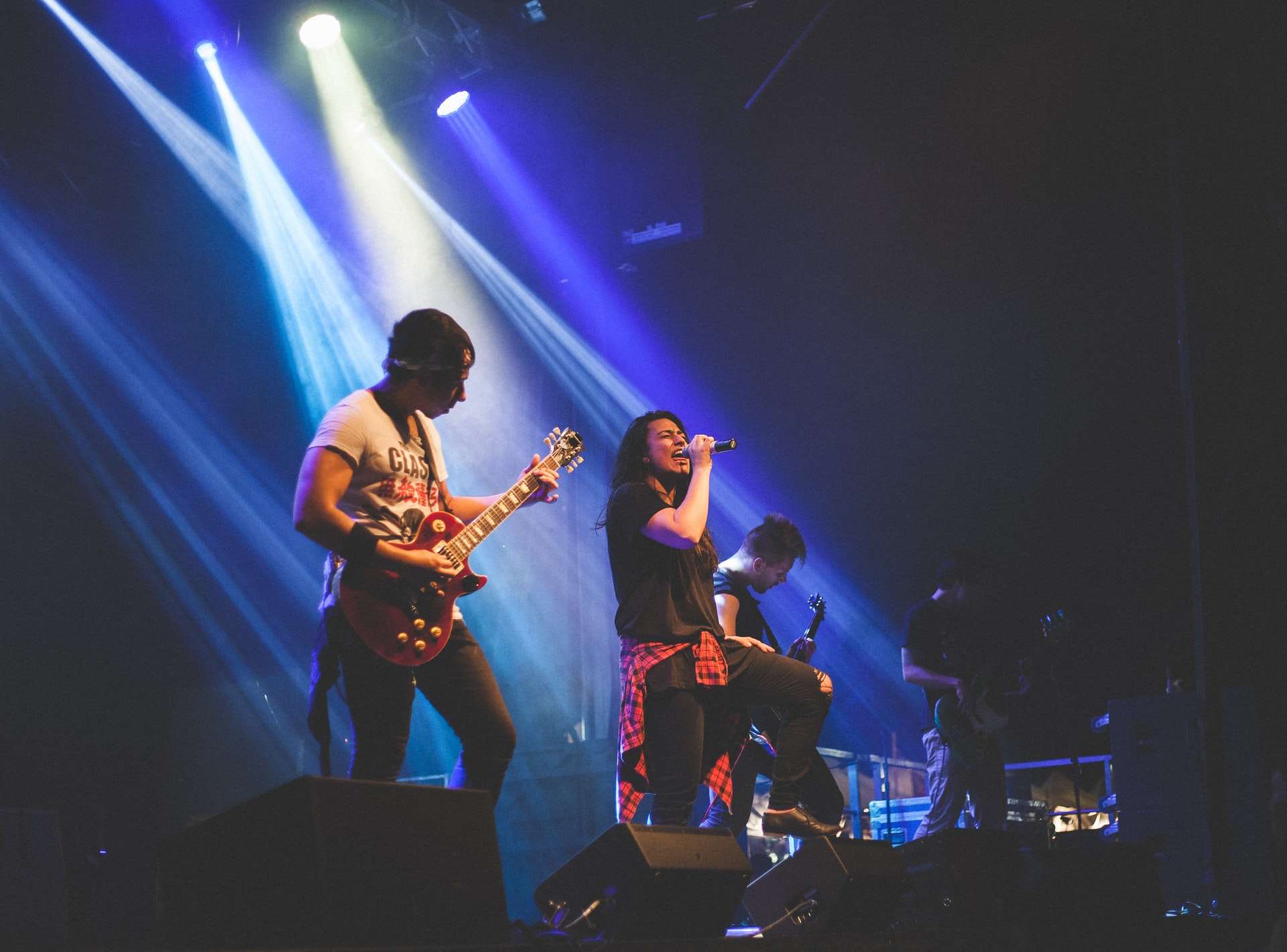 Un groupe de musique rock avec chanteur avec une chanteuse et 3 guitaristes a répondu à une annonce musicien pour jouer un concert sur scène sous le feu des projecteurs bleus.