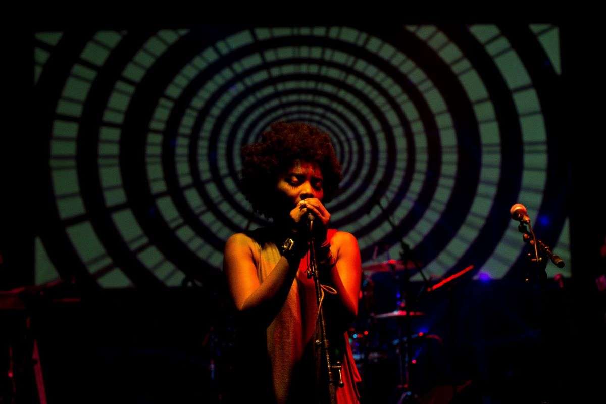 Plan concert d’une jeune chanteuse sur scène derrière un fond hypnotique.