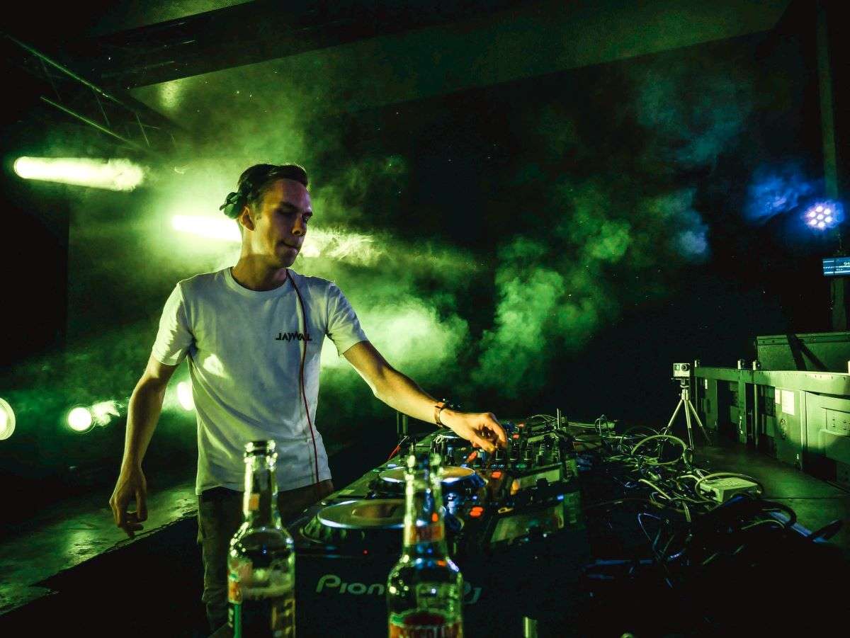 Plan concert d’un dj devant ses platines et son public éclairé de néons verts.
