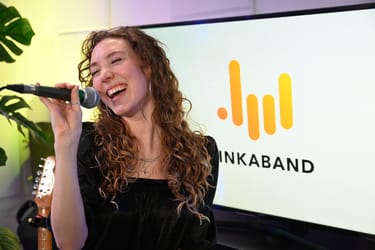 Une chanteuse se tient devant un micro en train de chanter sur scène, elle a le bras levé et la main sur le coeur.