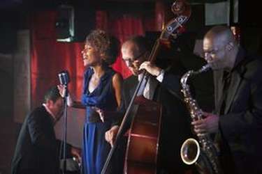 Groupe de jazz jouant un concert. Il est composé d'une chanteuse, d'un contrebassiste et d'un saxophoniste.