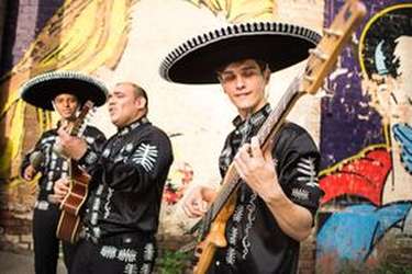 Groupe Latino en tenue traditionnelle de mariachi mexicain, jouant dans la rue devant un mur peint de la guitare.