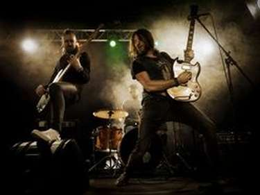 Groupe de Rock qui joue un concert sur scène avec le trio classique du rock : guitariste, bassiste et batteur se tenant devant des projecteurs.