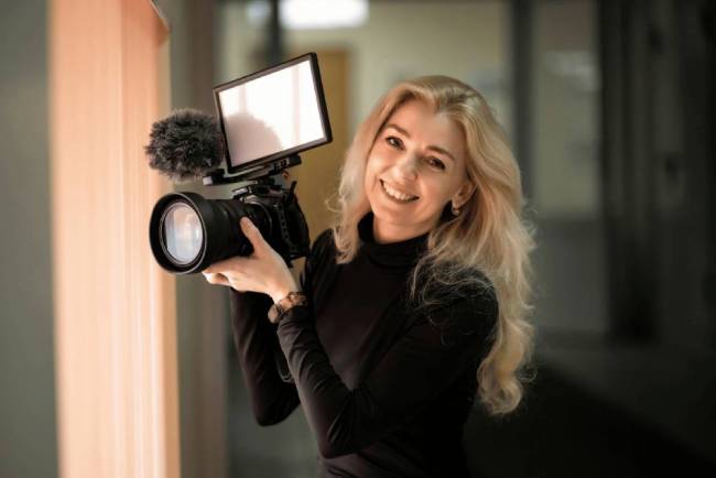 Vidéaste souriant tenant une caméra vidéo à la main avec un micro d'enregistrement et une lumière de tournage vidéo